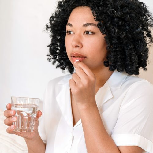 african american woman hold glas of water and taking medication from head ache or stomach pain. young female suffering from depression and has sedative pill. disease treatment concept