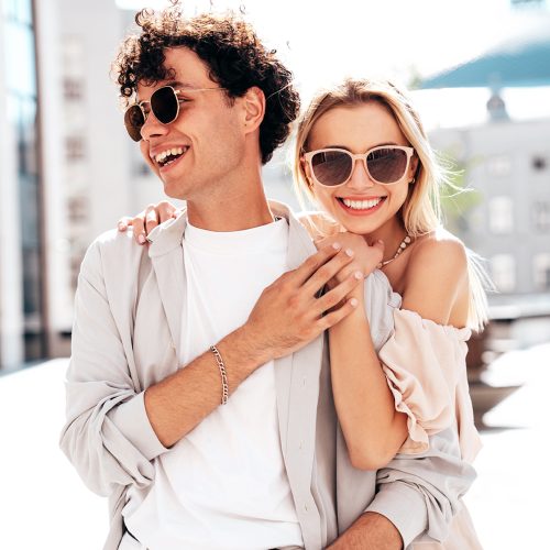 Young smiling beautiful woman and her handsome boyfriend in casual summer clothes. Happy cheerful family. Female having fun. Couple posing in the street background at sunny day. In sunglasses